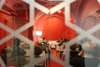 View through a decorative fence of a discussion panel inside a red room with attendees listening.