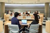 A business meeting is taking place in a modern classroom setting, with two individuals engaged in discussion in front of a laptop.