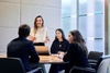 A business meeting with a woman presenting to three colleagues around a conference table.