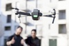 A drone hovers in front of two people giving a thumbs up.