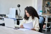 A woman with curly hair is focused on her work at a desk with a laptop and papers.