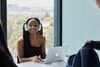A young woman with headphones smiles while working on a laptop in a modern office space.