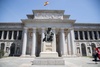 The image depicts the facade of a large building with classical architecture and a statue in the foreground.