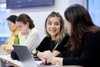 A group of students engaged in conversation and work at a table in a classroom setting.