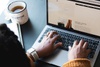 A person typing on a laptop with a cup of coffee nearby.