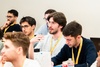 A group of young men engaged in a discussion at a conference, with one speaking and the others listening.