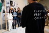 Three individuals pose for a photo at a display featuring various artistic works, while another person in a 'Plastic Free Oceans' shirt is seen from the back.