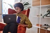 A person sitting in an orange armchair, using a laptop while focused on the screen.