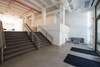 A modern interior space featuring a staircase with grey steps, white walls, and exposed red ceiling pipes.
