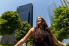 A young woman is smiling joyfully in front of tall buildings on a sunny day.