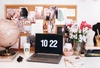A stylish and creative workspace featuring a laptop displaying the time, surrounded by decorative items and images on a cork board.