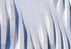 The image features a modern architectural facade with flowing, wave-like patterns in shades of white and blue.