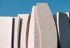 A modern architectural structure with abstract, wave-like surfaces against a blue sky.