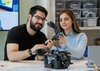 Two people are collaborating on a robotics project, focusing on a robotic arm.