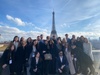 A large group of people posing together in front of the Eiffel Tower on a clear day.