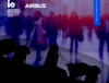 Silhouettes of military personnel in the foreground with a blurred crowd in the background, highlighted by blue and purple tones.