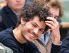 A young man with curly hair smiling and adjusting his hair in a public setting