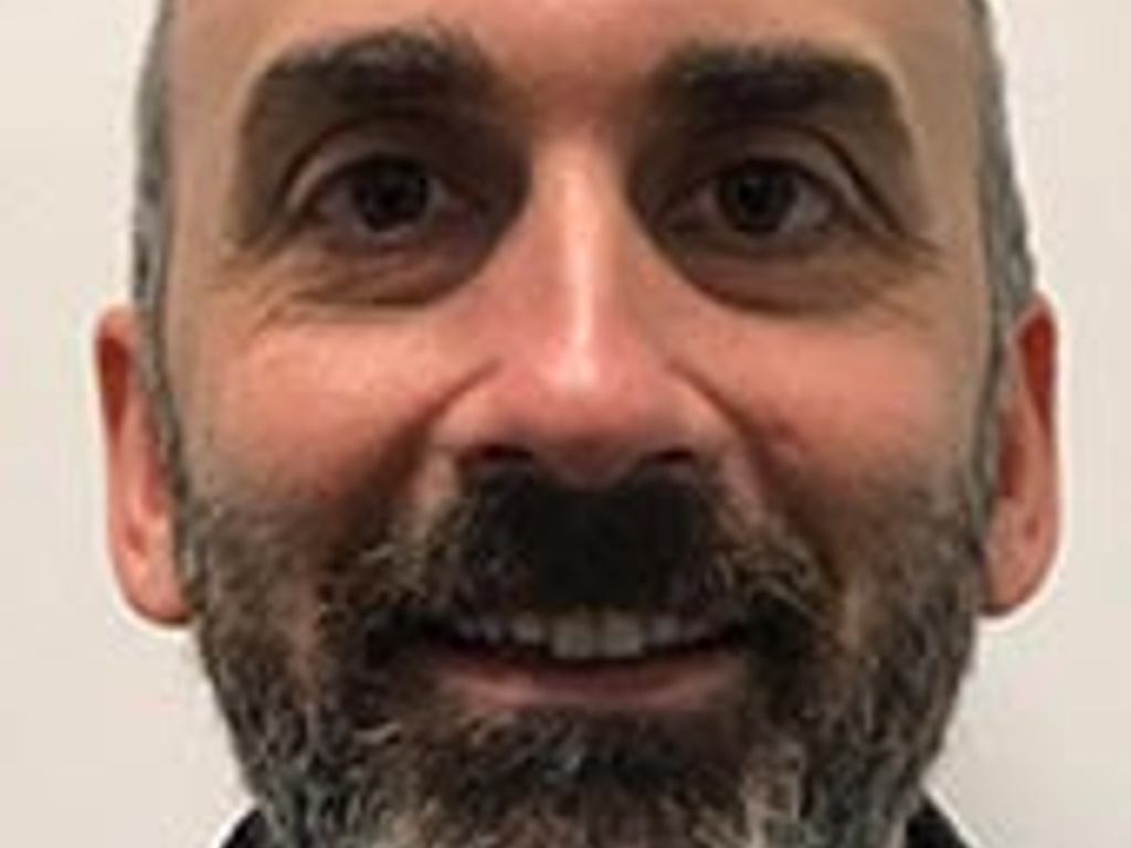 Close-up portrait of a smiling man with a beard, looking directly at the camera.