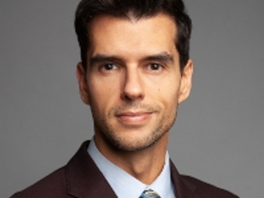 A professional portrait of a man in a dark suit and blue tie.