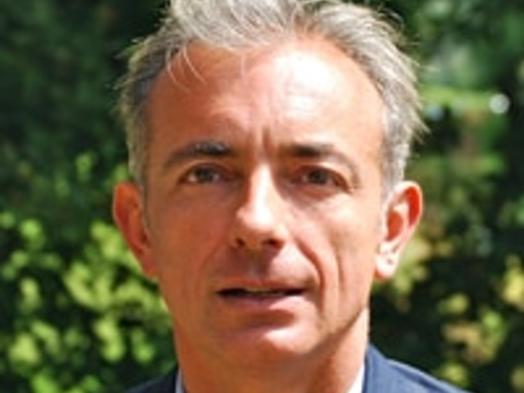 A portrait of a middle-aged man wearing a suit and tie, posing outdoors with trees in the background.