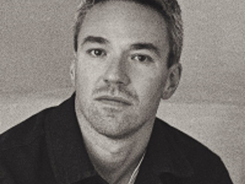 A black and white portrait of a middle-aged man looking directly at the camera with a neutral expression.