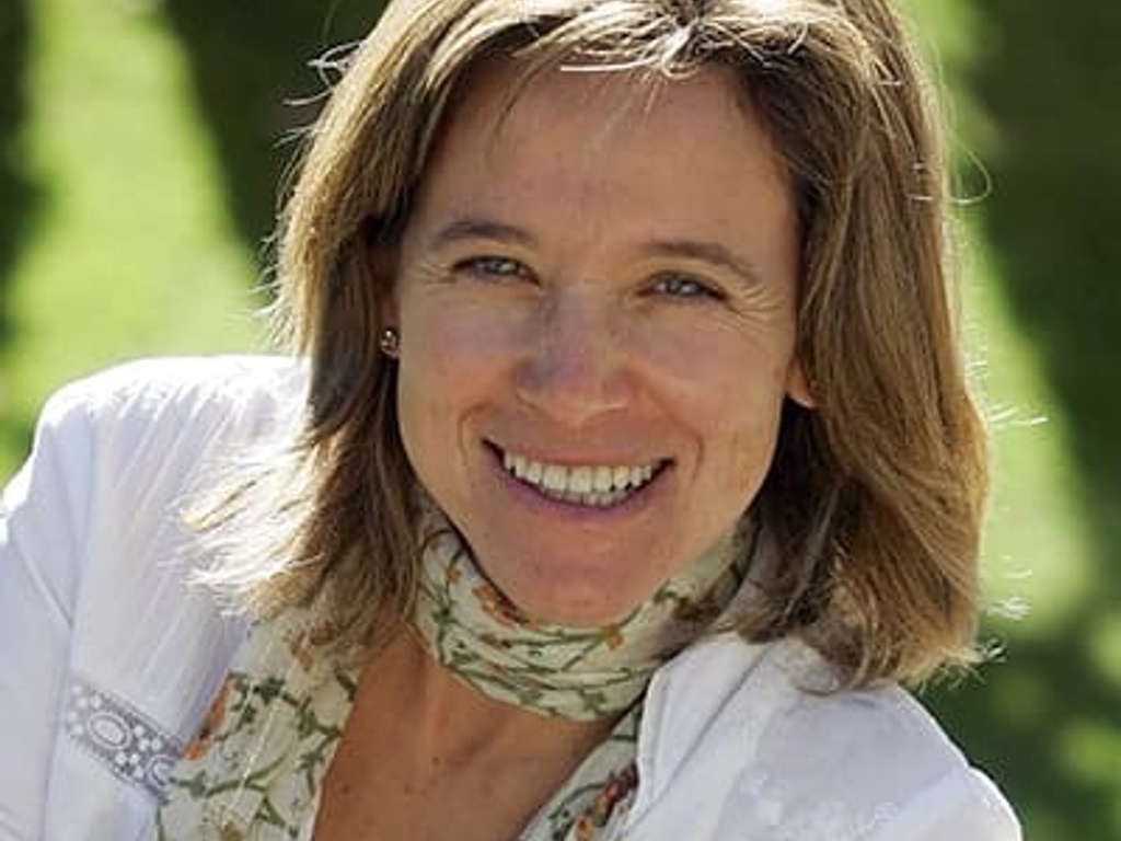 A smiling woman with shoulder-length brown hair, wearing a white blouse and a floral scarf, posing outdoors.