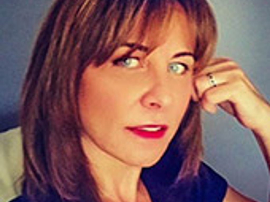 A close-up portrait of a woman with short brown hair, wearing a dark blue top and a thoughtful expression.