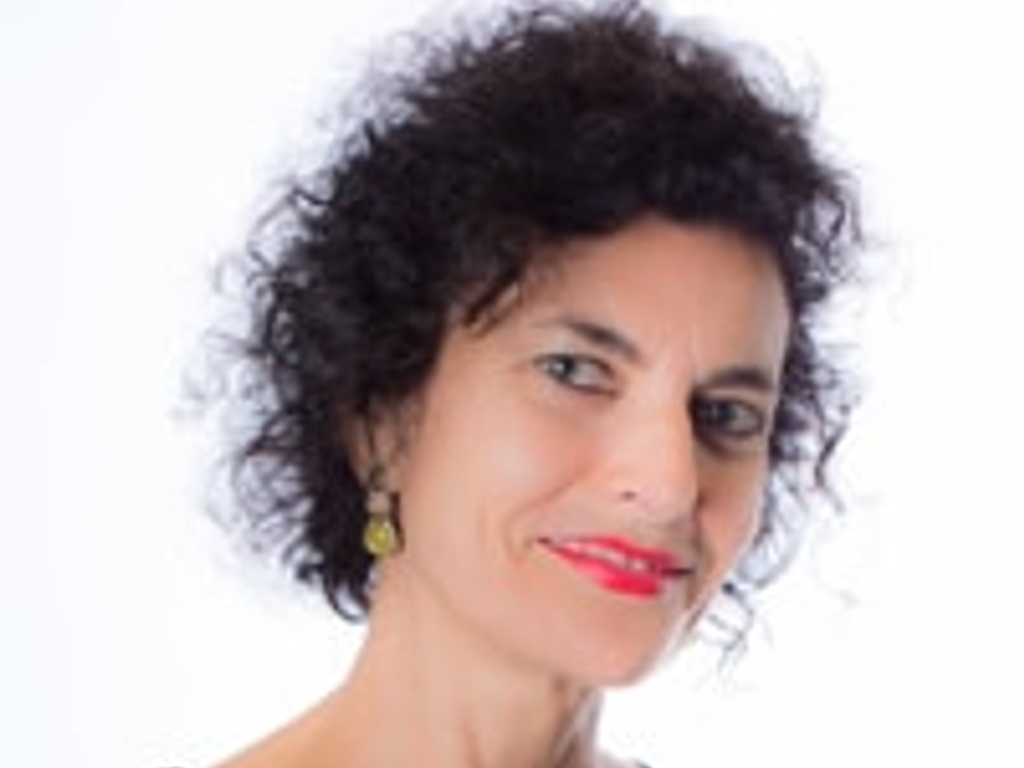 A portrait of a smiling woman with curly hair and a golden necklace.