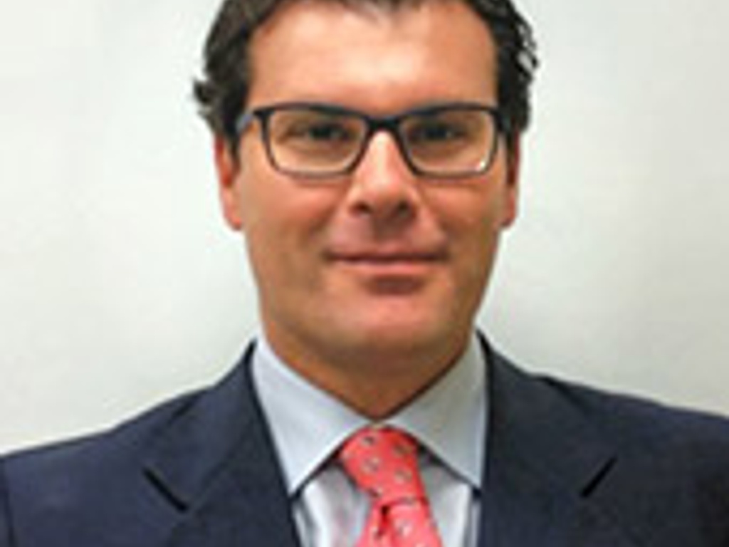 A professional portrait of a man wearing glasses, a blue suit, and a red tie.