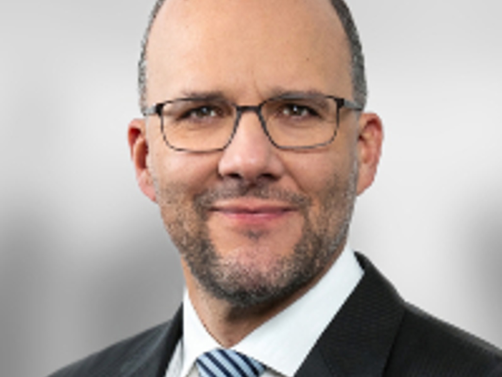 A portrait of a bald man wearing glasses and a suit with a striped tie.