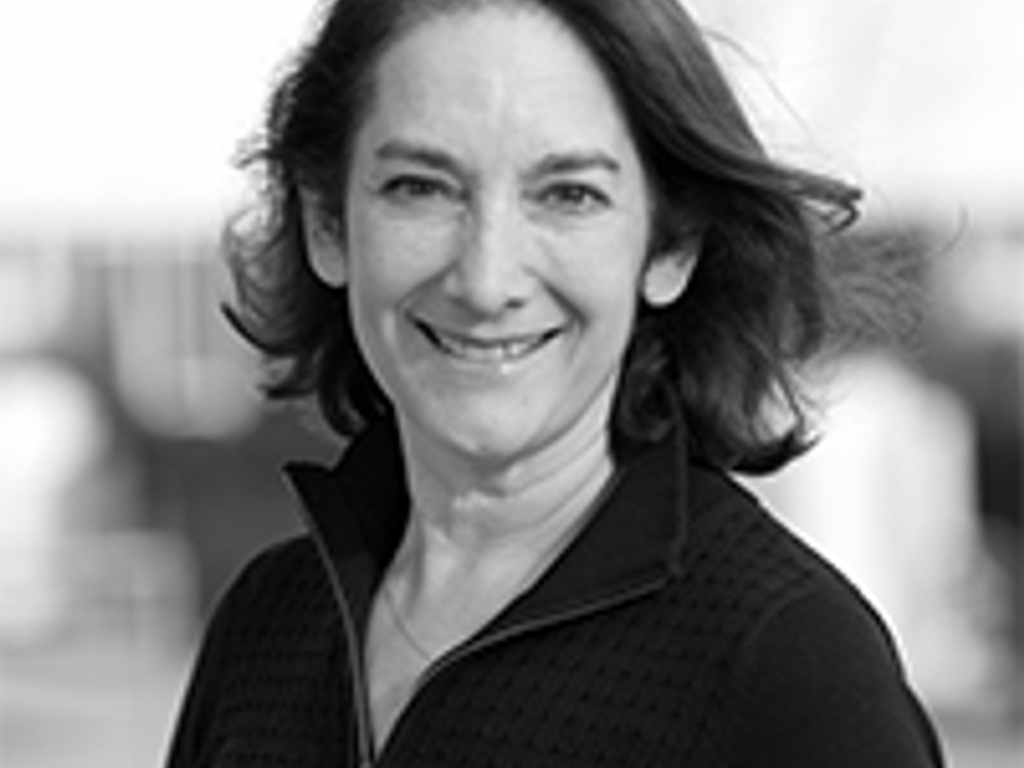 A black and white portrait of a smiling woman with shoulder-length hair, wearing a zip-up top, outdoors.