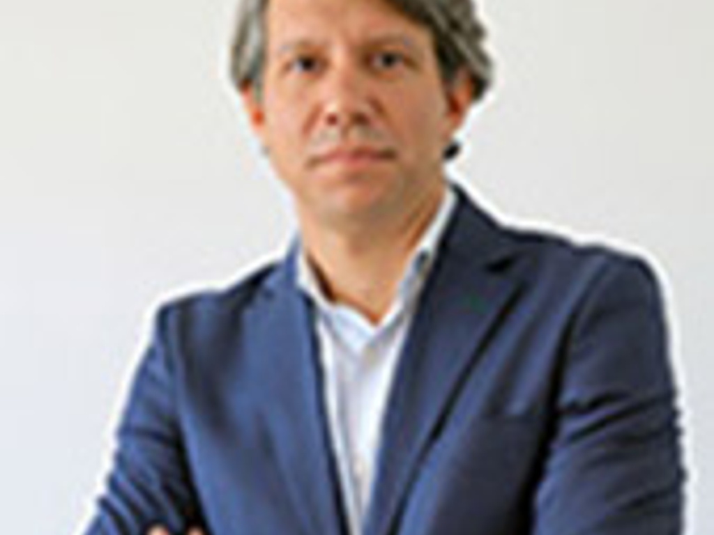 A professional man in a blue suit jacket standing with arms crossed in an office setting.