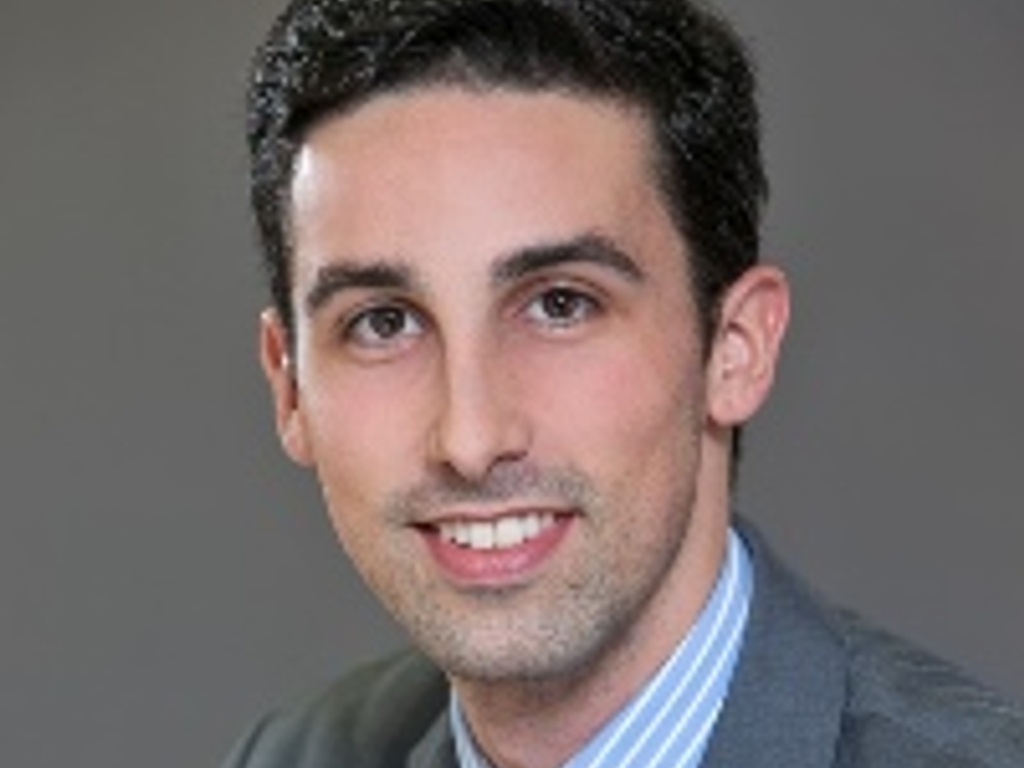 A professional headshot of a smiling man wearing a gray suit and blue tie.