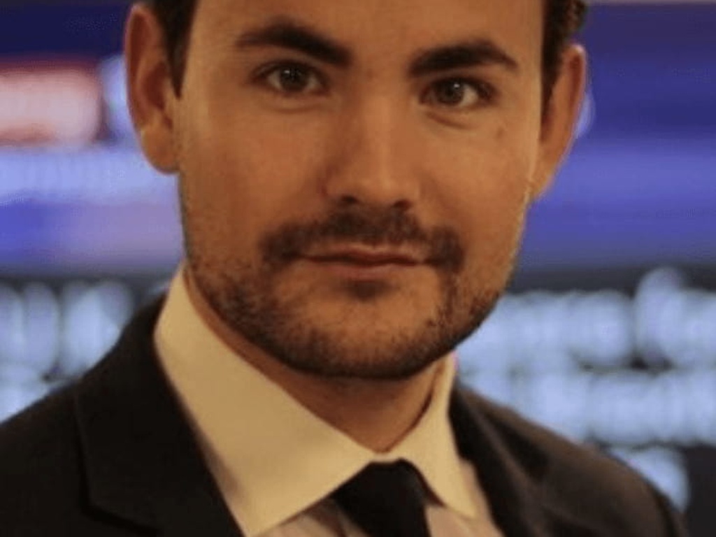 A portrait of a man with a beard, wearing a dark suit and tie, looking directly at the camera.