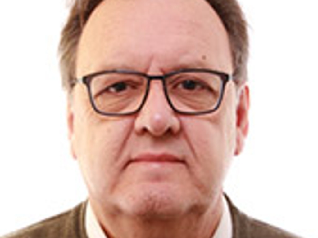 Portrait of a middle-aged man wearing glasses and a brown sweater, looking seriously at the camera.