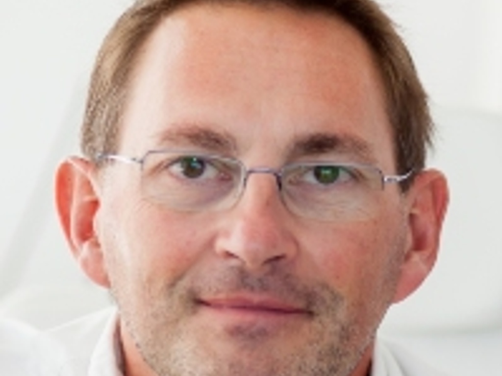 A close-up portrait of a middle-aged man with glasses smiling at the camera.