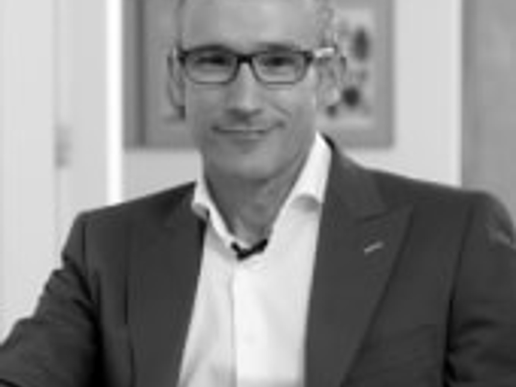 Black and white portrait of a smiling man wearing glasses and a suit.