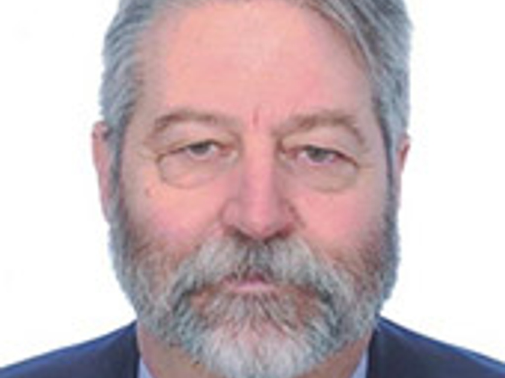 Portrait of a bearded middle-aged man with a serious expression, wearing a suit, on a neutral background.