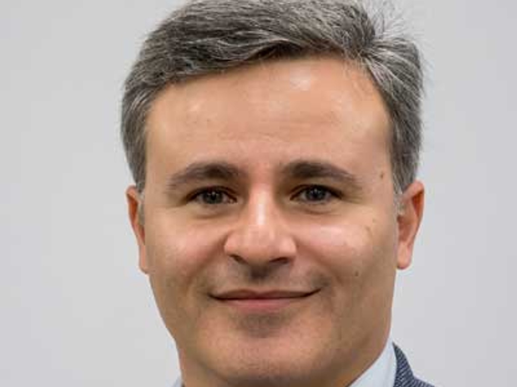 Portrait of a smiling man with gray hair, wearing a blazer and a collared shirt.