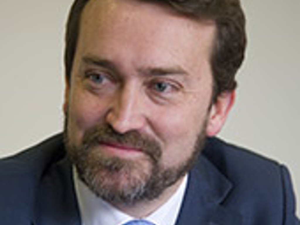A man in a blue suit and tie smiling slightly.