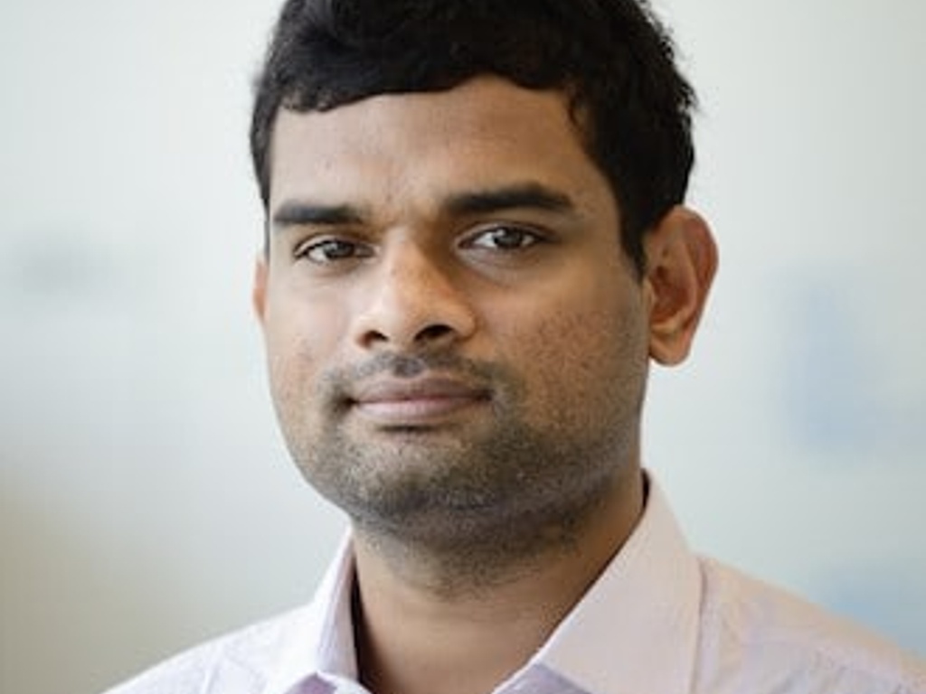 A portrait of a man in a light pink shirt, looking at the camera.