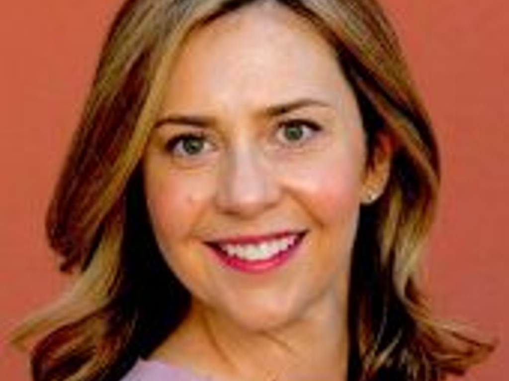 Portrait of a smiling woman with brown hair wearing a pink top against a red background.