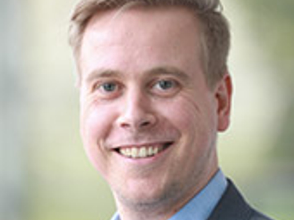 A professional portrait of a smiling man in a suit and tie.