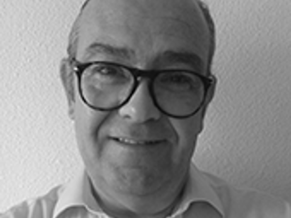 A black and white portrait of a smiling middle-aged man wearing glasses and a white shirt.