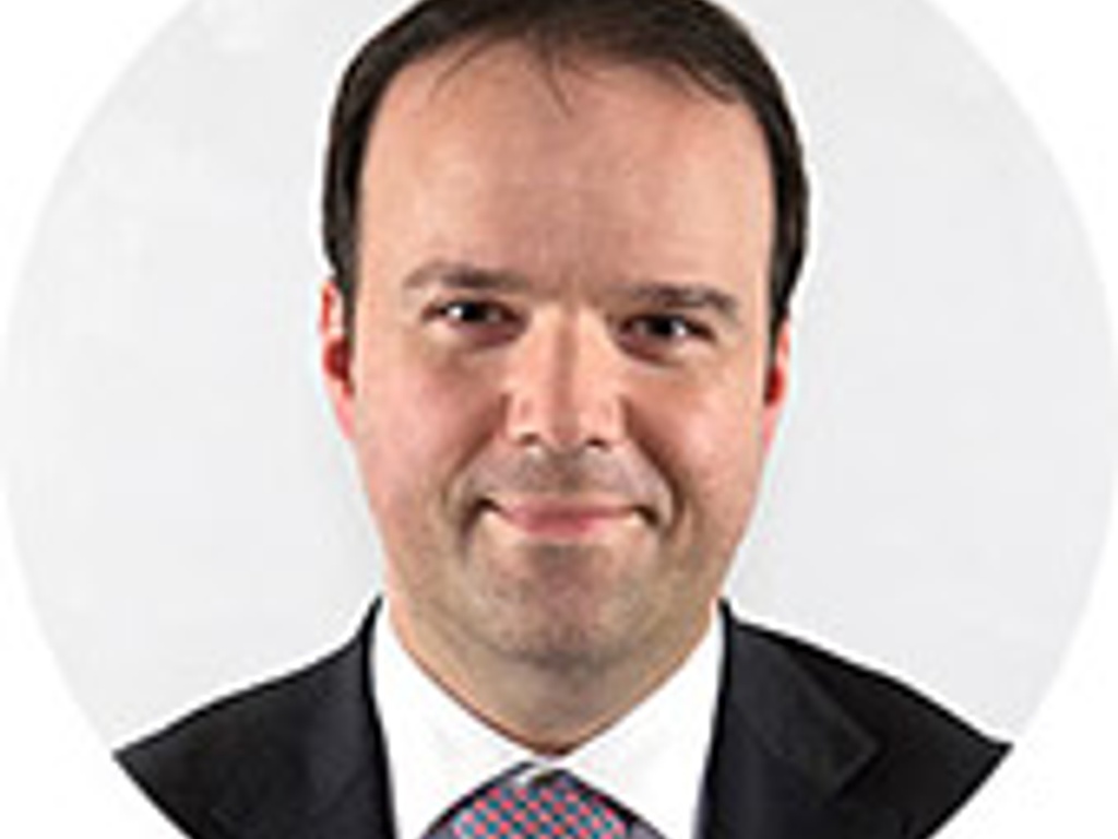 A portrait of a smiling man wearing a suit and tie with a plain background.