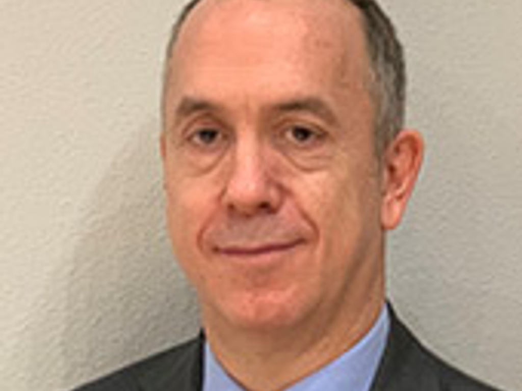 A professional middle-aged man in a suit and blue tie smiling at the camera.