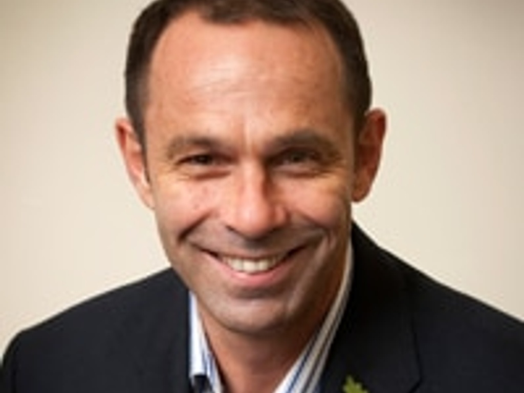 A smiling man wearing a suit and a red poppy pin on his lapel.