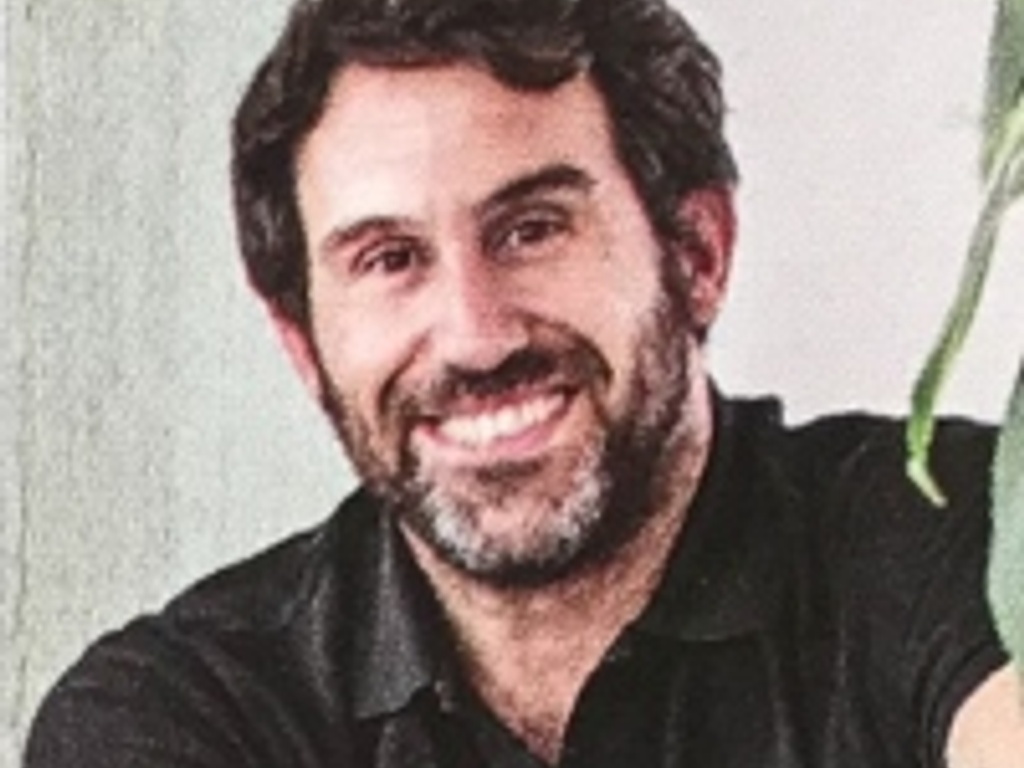 A smiling man with a beard wearing a black polo shirt.