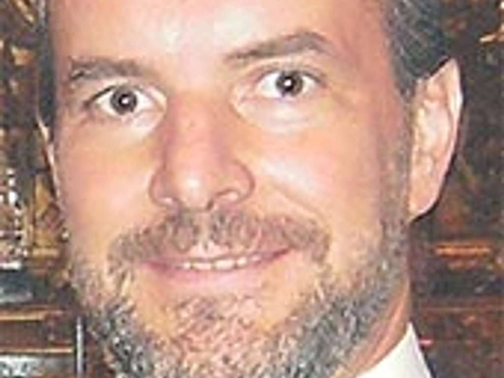 Portrait of a smiling man with a beard and mustache, wearing a black suit and tie.