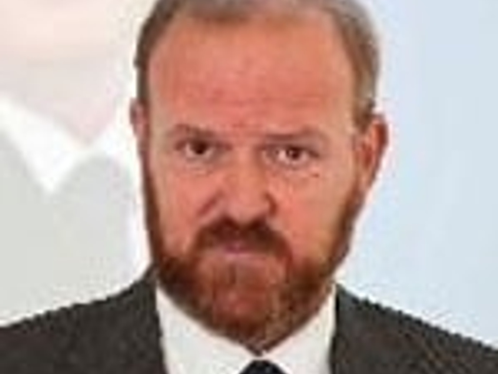 A man in a formal suit with a beard looking serious.